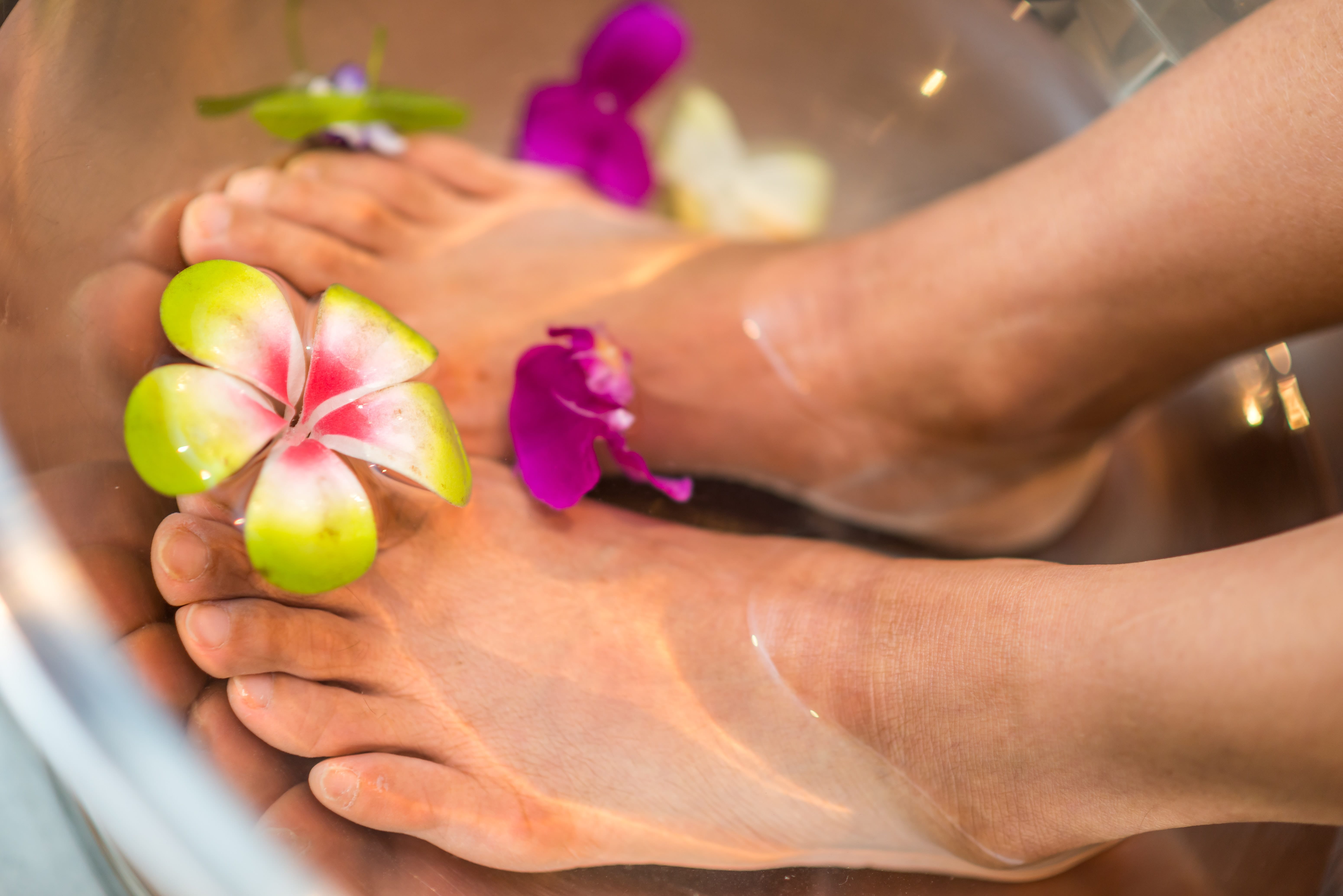 womans feet in bowl of water with flowers